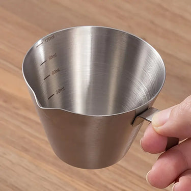 Stainless steel measuring cup held by a hand on a wooden surface